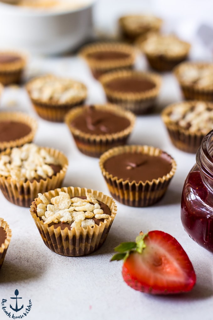 Peanut Butter Cups with rice cereal and plain chocolate peanut butter cups on a white background with a strawberry half in front.