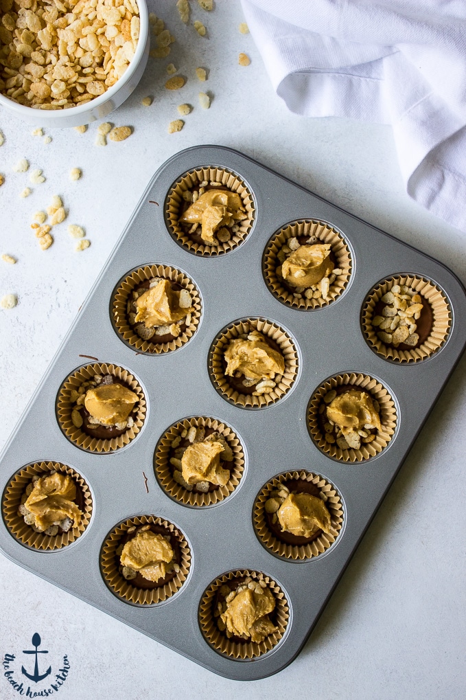 Overhead photo Peanut Butter Cups in muffin tin with small white bowl of crispy rice cereal in background.