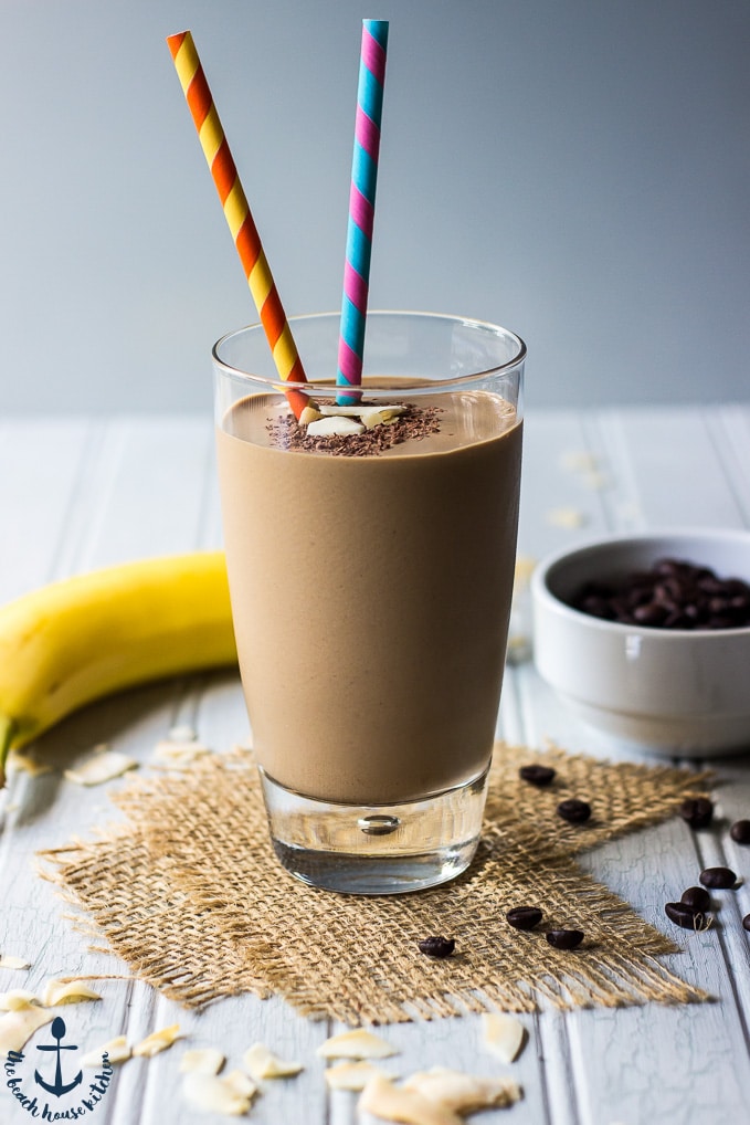Chocolate Coconut Coffee Smoothie with two colorful straws, on top of two pieces of burlap ribbon with a banana in background.