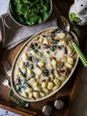 Mushroom Florentine Gnocchi on a wooden tray with a colander of fresh spinach.