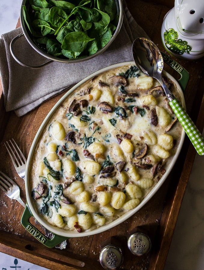 Mushroom Florentine Gnocchi on a wooden tray with a colander of fresh spinach.