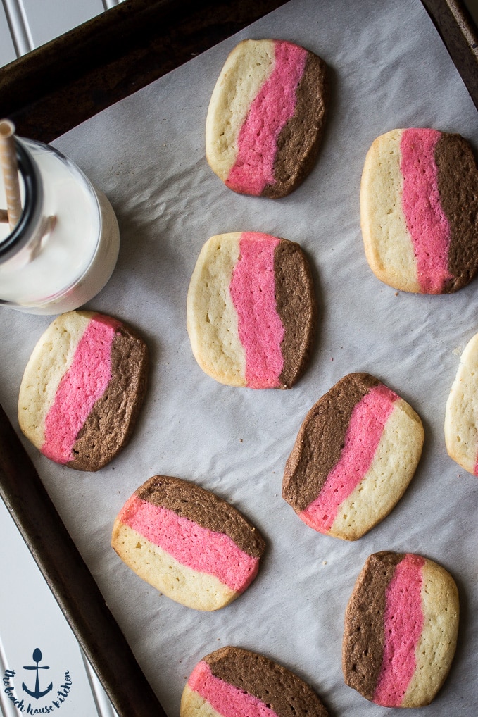 Overhead photo of baked pink, white and brown Neapolitan Butter Cookies on baking sheet with bottle of milk.