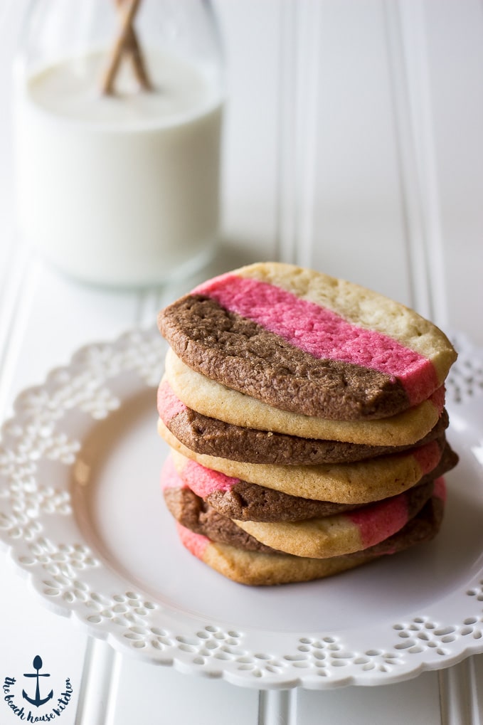 Stack of Neapolitan Cookies on white plate with lace edge with bottle of milk in background.
