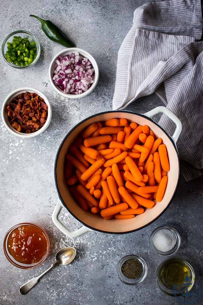 Overhead photo of large pot of carrots, bowls of jalapenos, red onion, bacon, apricot glaze, salt and pepper.