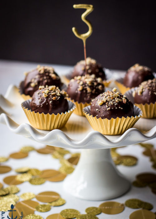 Pecan Pie Truffles in gold foil cups on a white cake pedestal with a number 3 pick in center truffle.