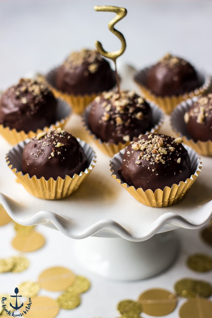 Pecan Pie Truffles in gold foil cups on a white cake pedestal with a number 3 pick in center truffle.