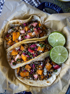 Three chipotle sweet potato quinoa tacos in a blue dish lined with brown parchment paper and a sliced lime.