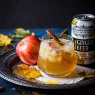The Fall Dark 'N' Stormy cocktail on a silver tray with an apple and a can of ginger beer.