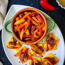Sweet Pepper and Chorizo Bruschetta Polenta Bites on a white oval platter with a green bowl filled with red and yellow pepper strips