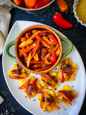Sweet Pepper and Chorizo Bruschetta Polenta Bites on a white oval platter with a green bowl filled with red and yellow pepper strips