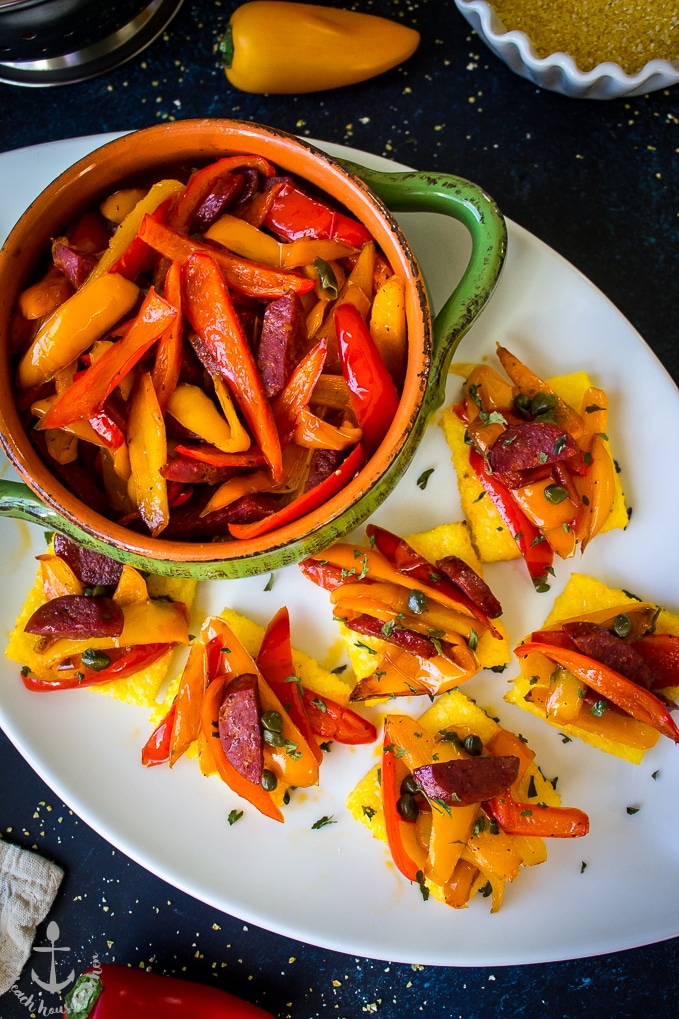 Sweet Pepper and Chorizo Bruschetta Polenta Bites on a white oval platter with a green bowl filled with red and yellow pepper strips.