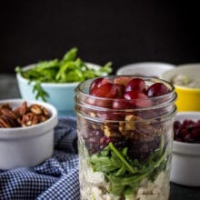 Turkey Salad with Grapes, Pecans and Cranberries in a Jar with pecans and argula in white bowls and blue and white checked napkin.