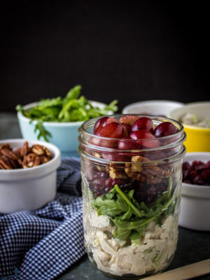 Turkey Salad with Grapes, Pecans and Cranberries in a Jar with pecans and argula in white bowls and blue and white checked napkin.