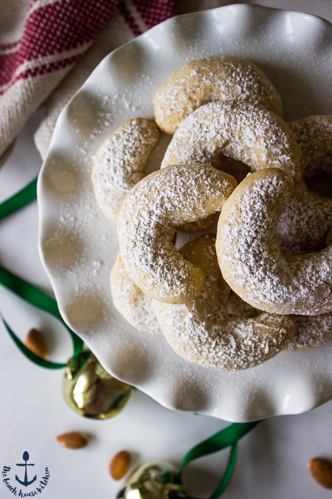 Almond Crescents on white plate dusted with confectioners' sugar with jingle bells in background.