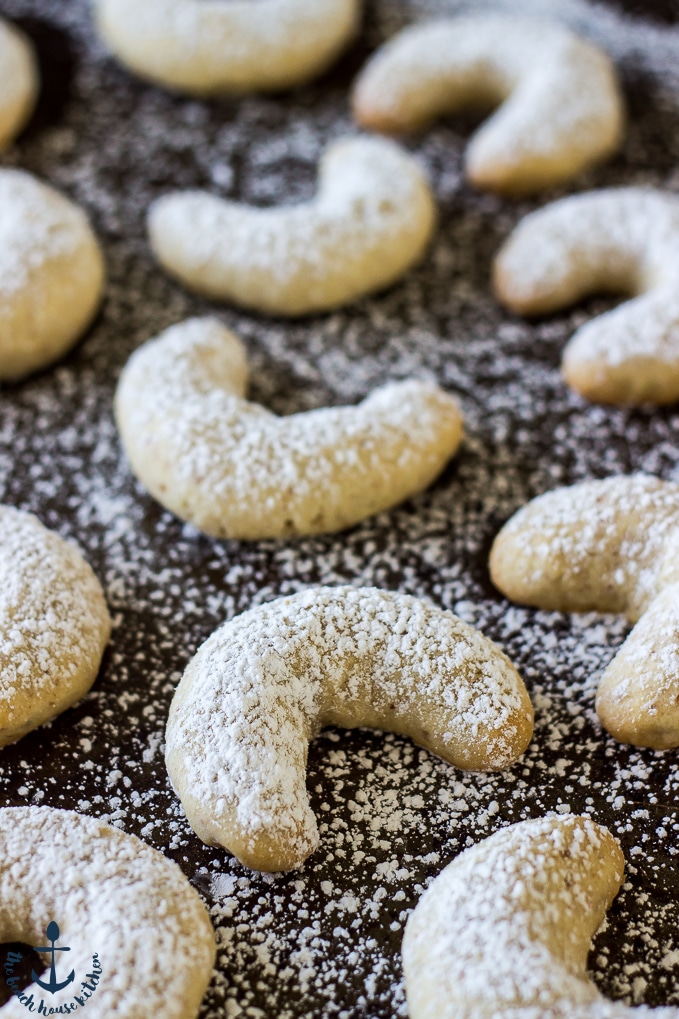Almond Crescents on dark baking sheet dusted with confectioners' sugar.