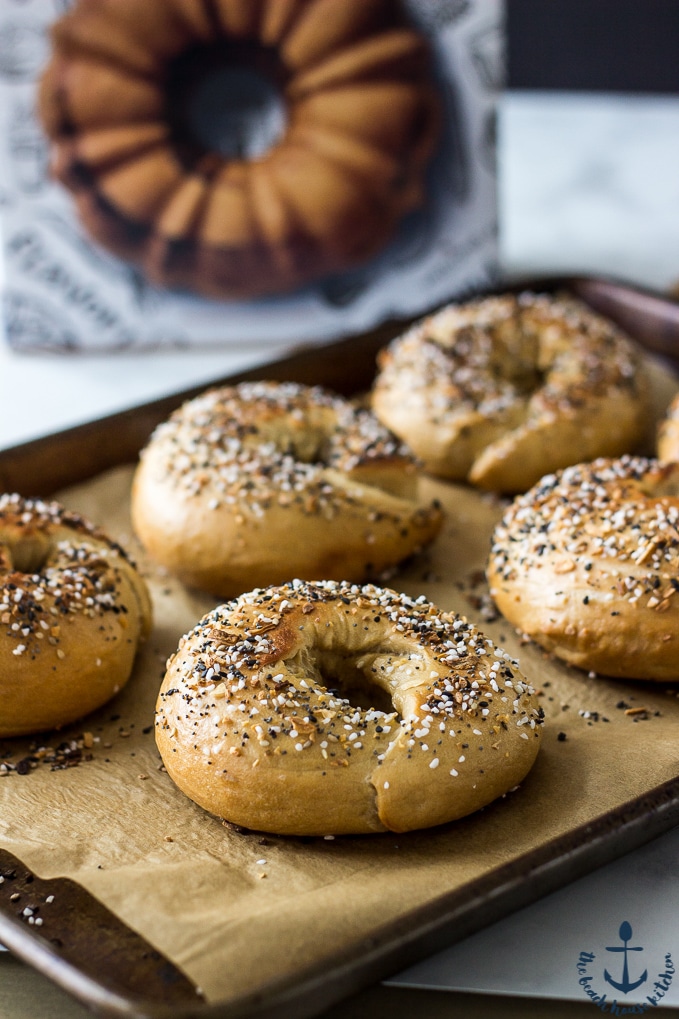 Everything Bagels on a baking sheet lined with parchment paper with cookbook in background.