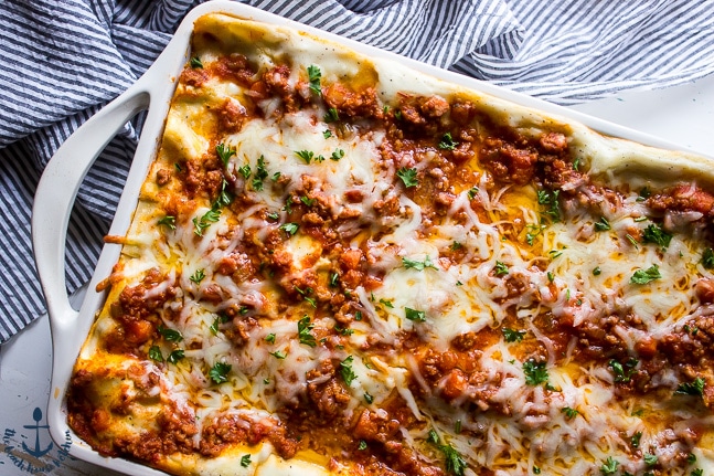Overhead shot of lasagna bolognese in a white baking pan with a blue and white striped dish cloth