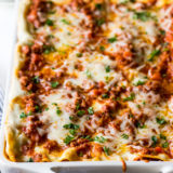 Lasagna Bolognese in a white baking dish with a blue and white striped napkin