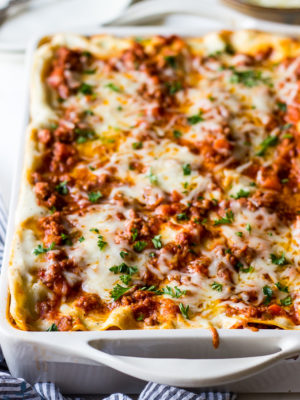 Lasagna Bolognese in a white baking dish with a blue and white striped napkin