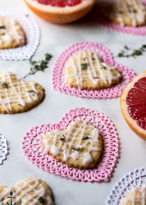 Pink Grapefruit and Thyme Shortbread Hearts on heart doilies with thyme leaves and pink grapefruit in background.