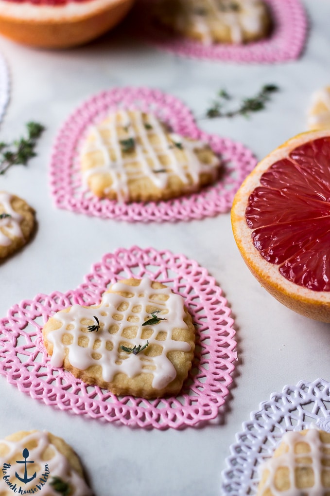 Pink grapefruit and thyme shortbread heart cookies on heart doilies with pink grapefruitsand thyme springs.