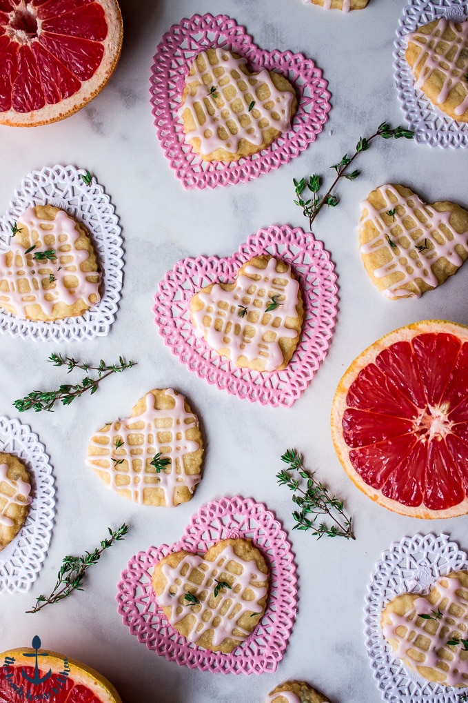 Overhead photo Pink Grapefruit and Thyme Shortbread Heart cookies on pink and white Valentine heart doilies with sprigs of thyme and pink grapefruit.