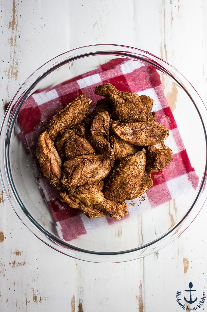 Overhead shot of wings coated in spicy rub in glass bowl on red and white checked napkin.