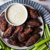 Overhead shot of spicy baked spicy wings with white bbq sauce on tray with celery and beer and lime in background.