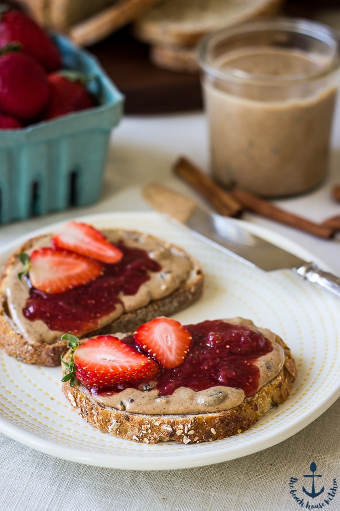 An open face Cinnamon Raisin Almond Butter and Strawberry Chia Jam sandwich on a white plate.