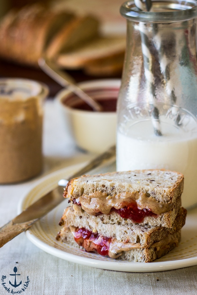 A Cinnamon Raisin Almond Butter and Strawberry Chia Jam sandwich on a plate with a bottle of milk in the background.