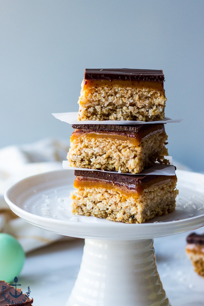 A stack of three Gluten-Free Coconut Dream Bars on a white pedestal cake plate.