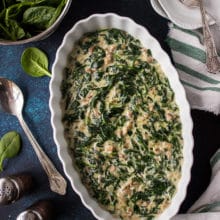 Overhead photo of Creamed Spinach in white oval dish on a blue background.