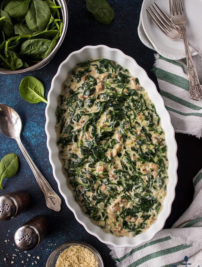 Overhead photo of Creamed Spinach in white oval dish on a blue background.