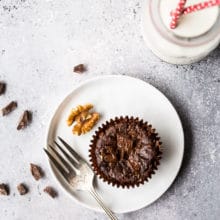 An overhead photo of a Double Chocolate Brownie Cupcake on a white plate with a silver fork and a bottle of milk with two straws