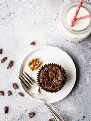 An overhead photo of a Double Chocolate Brownie Cupcake on a white plate with a silver fork and a bottle of milk with two straws
