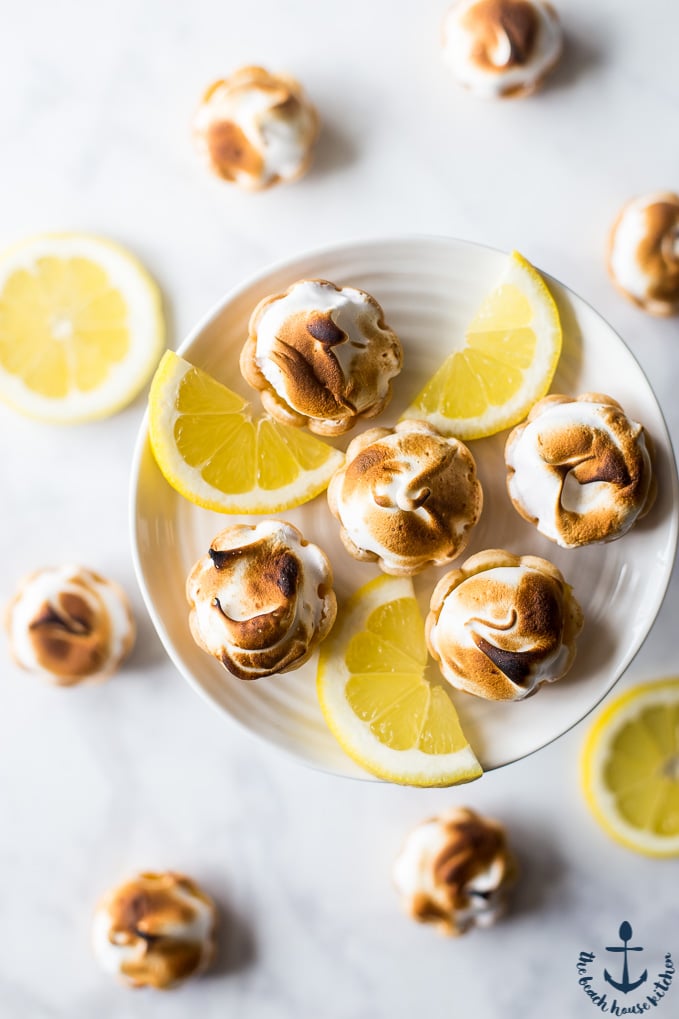 Overhead photo of Mini Lemon Meringue Pies with lemon slices on a white cake plate