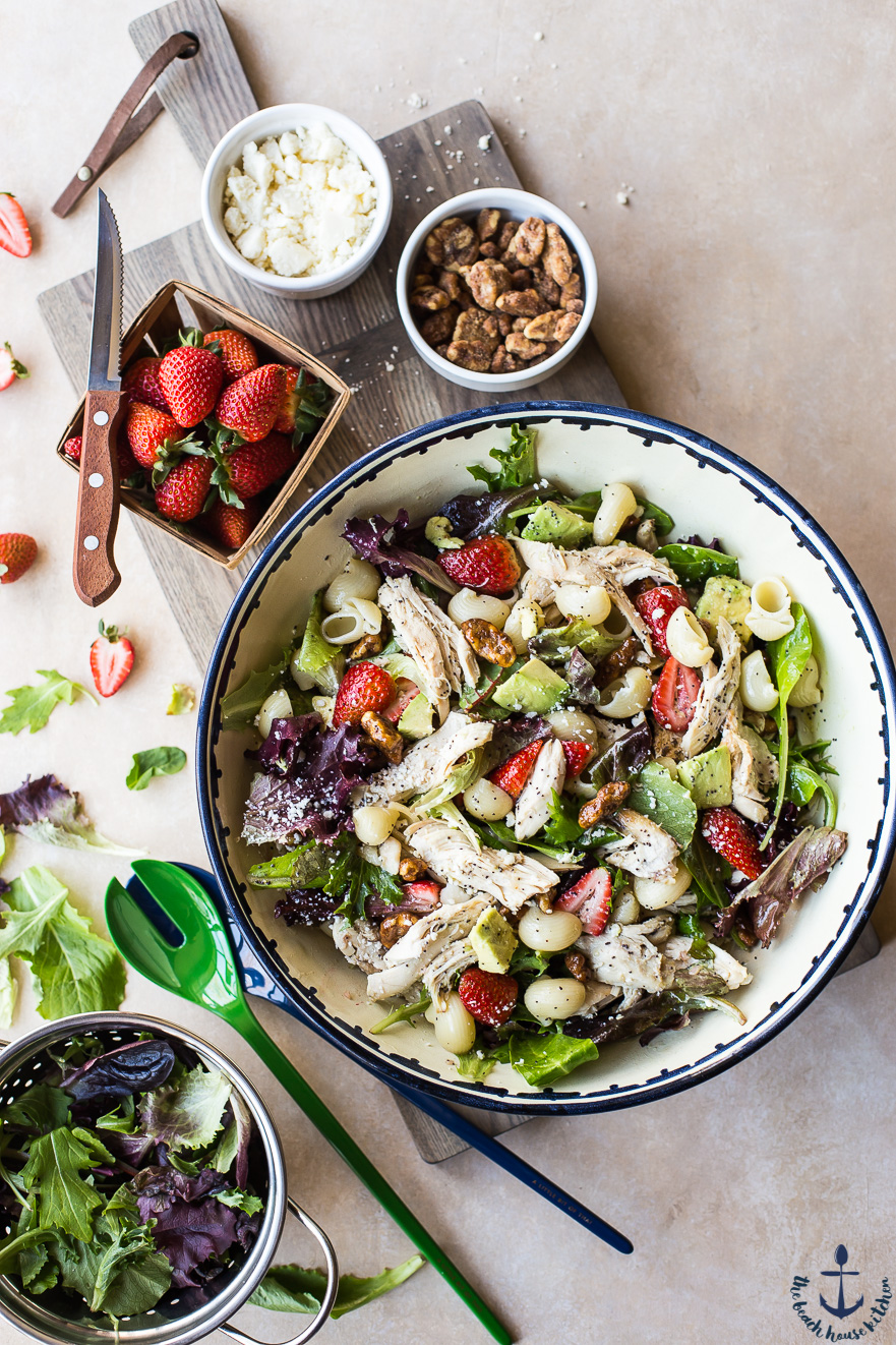 Overhead photo Chicken Strawberry Avocado Pasta Salad in a bowl with a basket of strawberries 