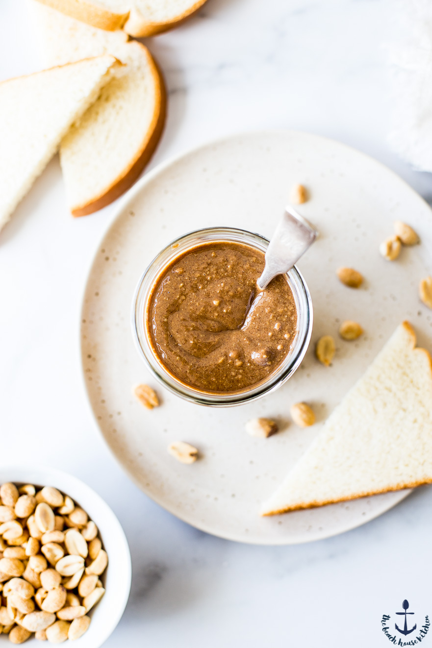 Overhead photo of a jar of cappuccino peanut butter with a silver spoon in in on a plate with a slice of bread
