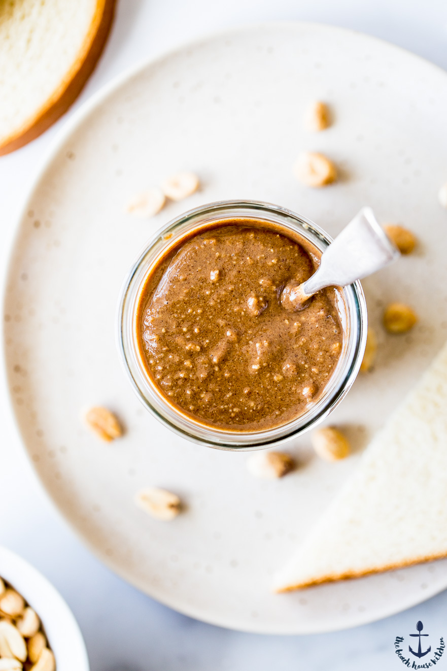 Overhead photo of a jar of cappuccino peanut butter with a silver spoon in in on a plate with a slice of bread