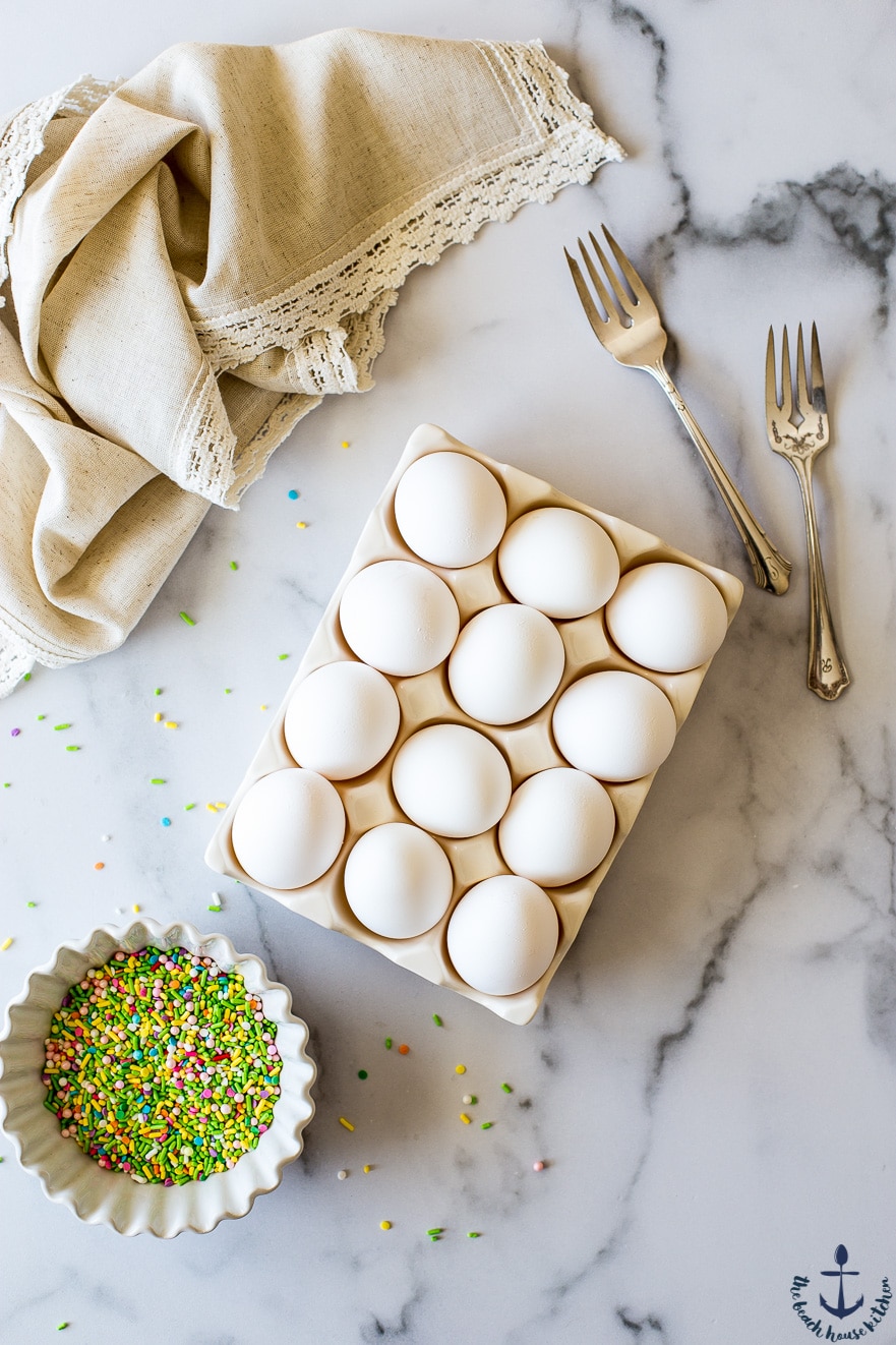 Overhead photo of a dozen eggs, two forks and a bowl of sprinkles