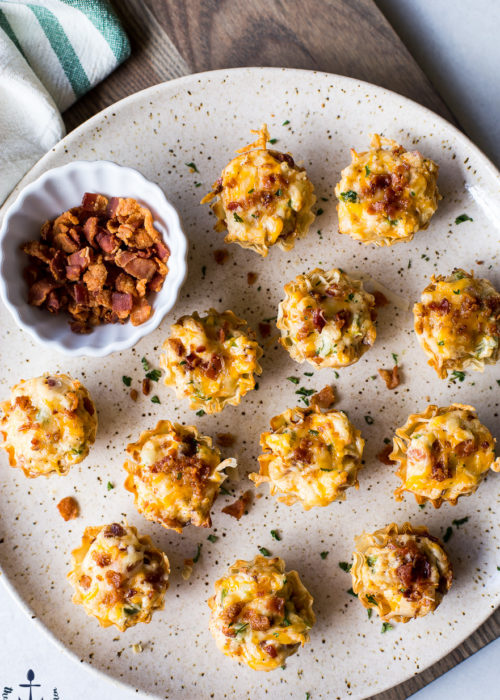 Overhead photo of Jalapeno Popper Pastry Bites on a plate with a small bowl of bacon bits.