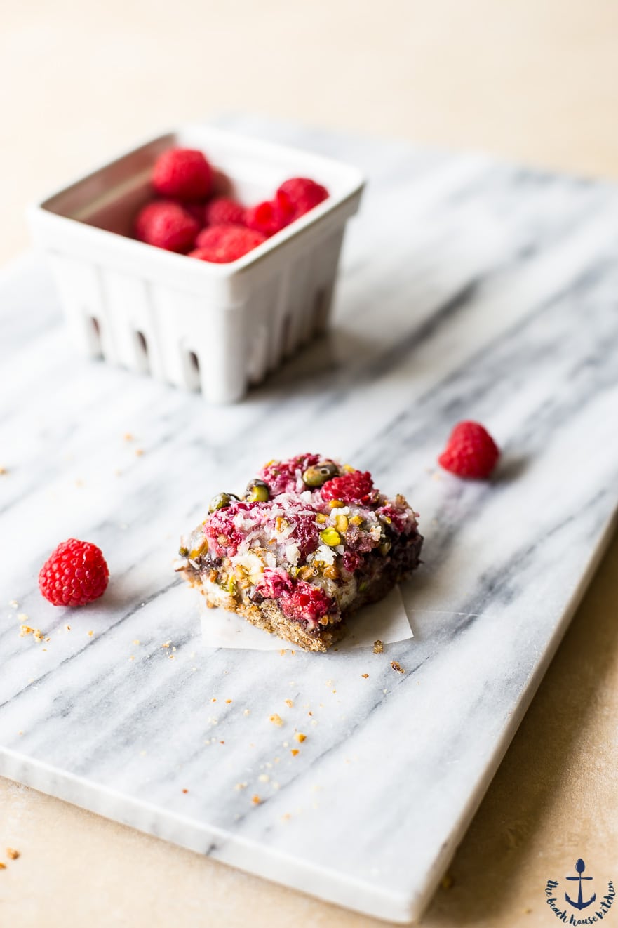 Photo of one raspberry pistachio bar on a marble board with container of raspberries