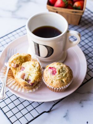 Strawberry lemon muffins on a plate with a cup of coffee and a small crate of strawberries