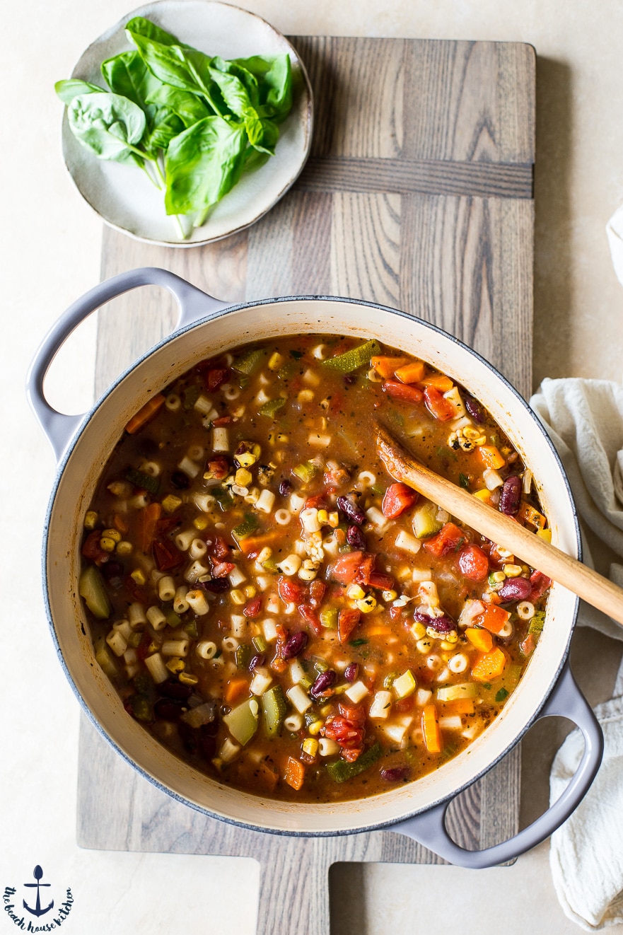 Overhead photo of summer minestrone soup in pot on wooden board