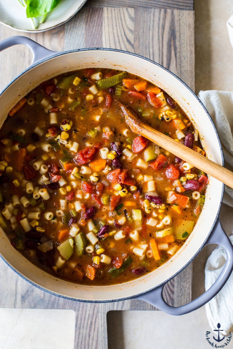 Overhead photo of summer minestrone soup in pot on wooden board