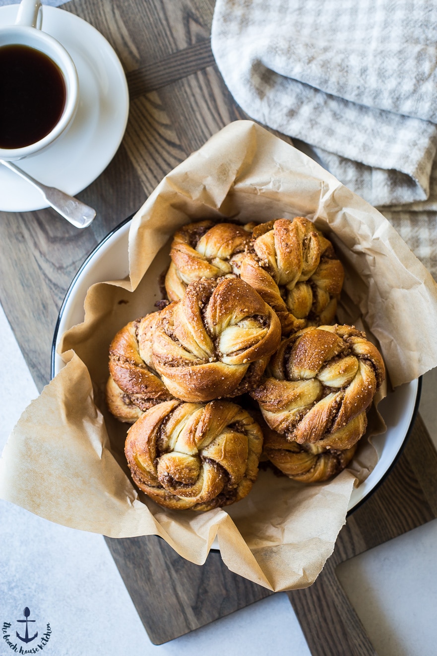 Overhead photo of Cinnamon Pecan Knots in dish with cup of coffee