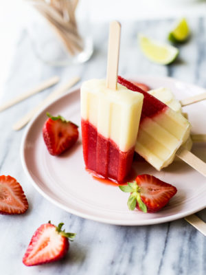 Miami Vice Boozy Popsicles on a pink plate surrounded by a few halved strawberries