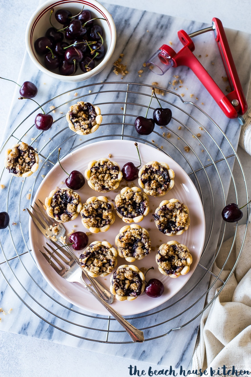 Overhead photo of streusel topped cherry pie bites on a pink plate with forks and cherries