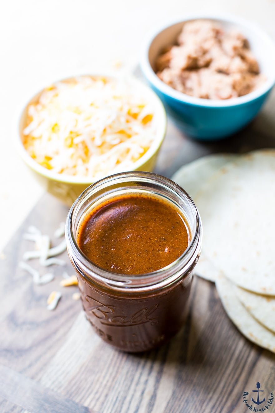 Enchilada sauce in a jar with shredded cheese and another side blurred in the background