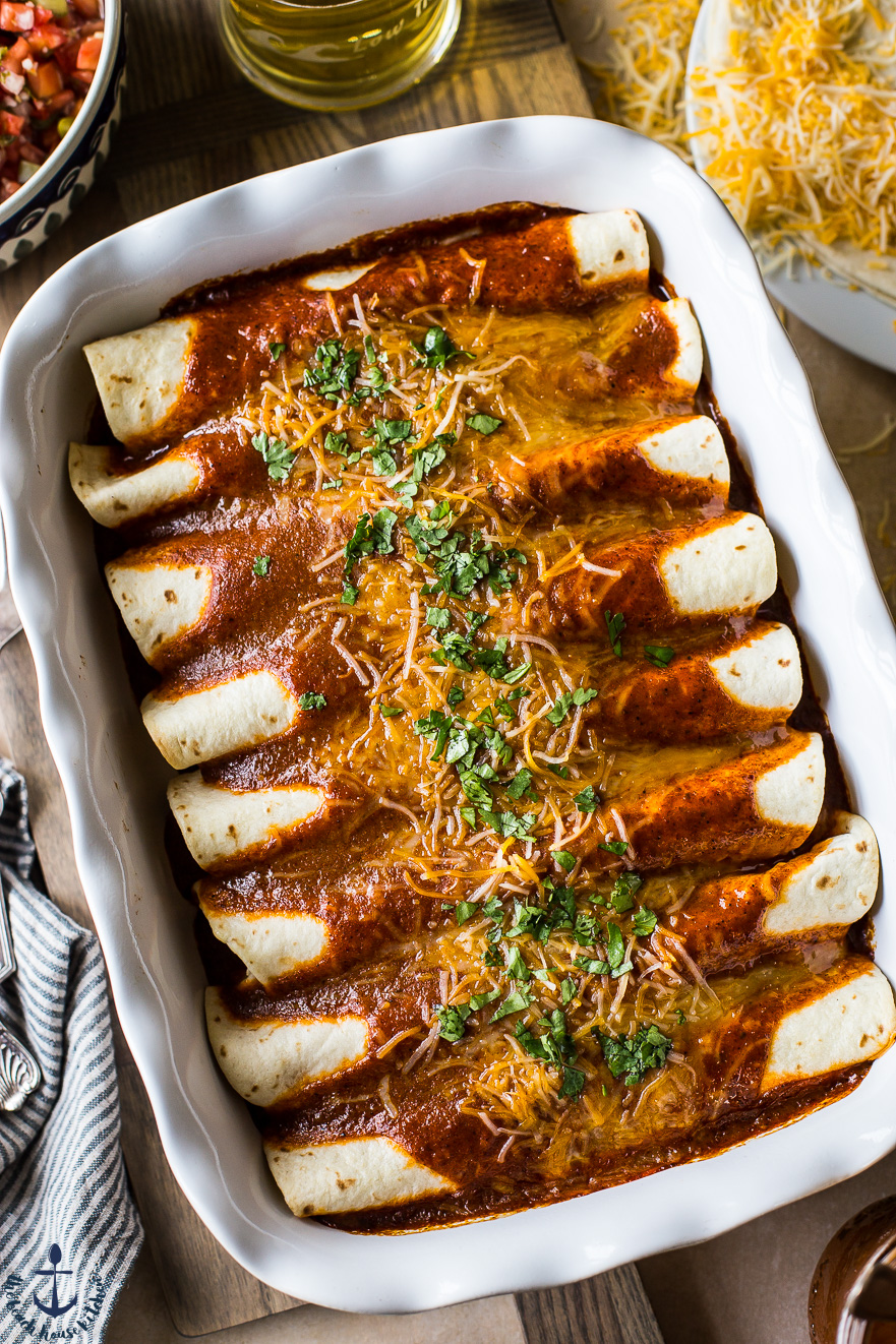 Overhead photo of Homemade Easy Beef Enchiladas in a long white dish with a few sides around it